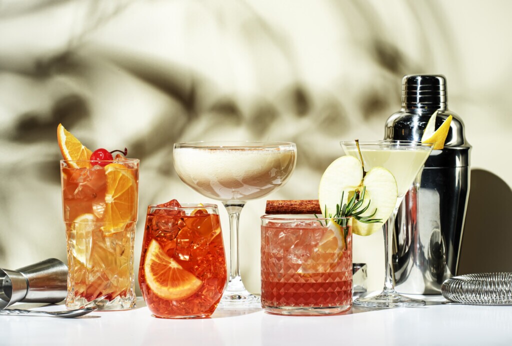 Cocktail party. Bright fruity and citrus alcoholic drinks with gin, vodka, vermouth and juice. Beige background, hard light, shadow pattern