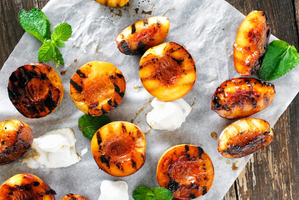 Honey grilled peaches served with mint leaves and ice cream top view, placed on a baking sheet on a table. 