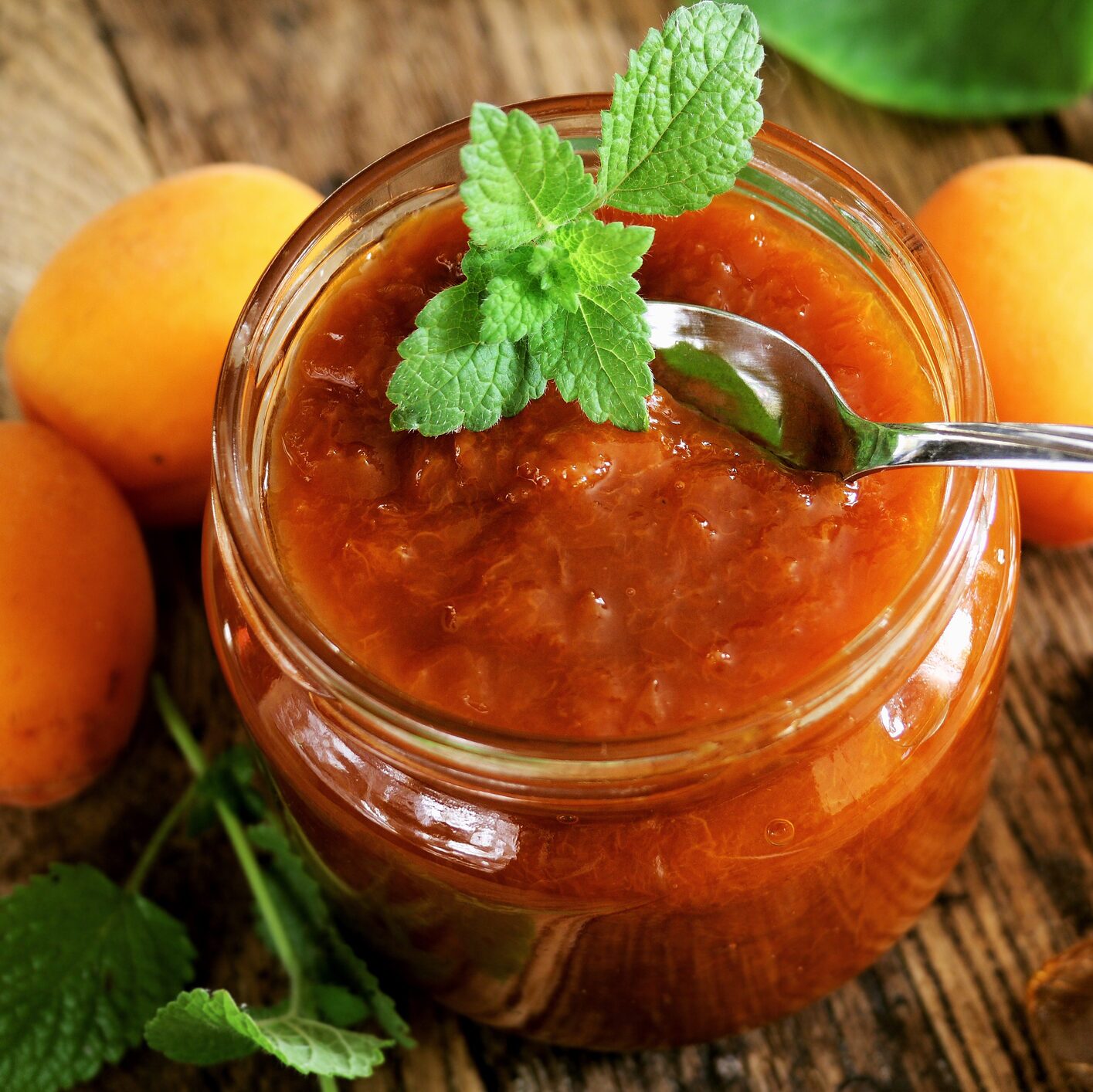 A spicy peach chutney in a mason jar and topped with a mint lead on a wooden table. 