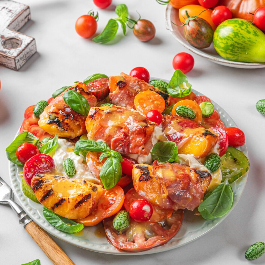 A white plate with a summer salad. The salad includes grilled peaches, vegetables, and cheese.
