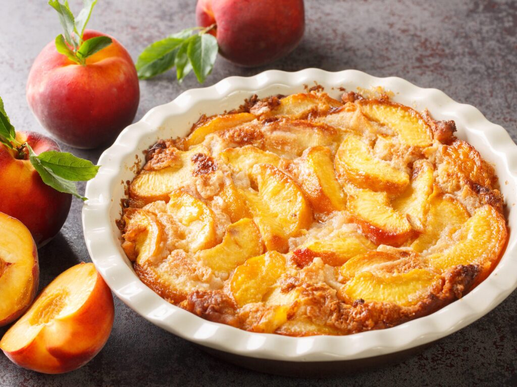 A southern-style peach cobbler in a round ceramic pie dish. The cobbler has a golden brown crust and is bubbling slightly. 