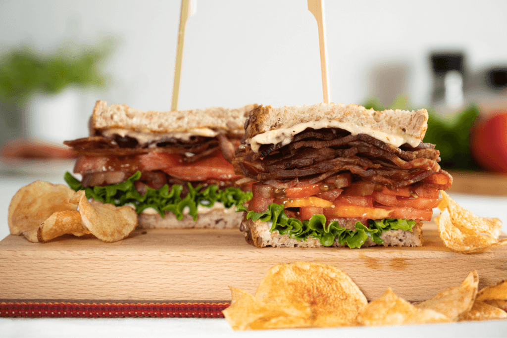 The image shows twqo halves of a classic BLT sandwich cut in half. The sandwiches are made with a multigrain or wheat bread and layered with lettuce, sliced tomato, crispy bacon, and herb mayo. Both sandwich halves have a toothpick in them.