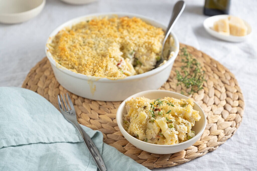 Leftovers Recipe: The image shows a round white casserole dish filled with creamy chicken tetrazzini. A portion has been scooped out and is in a small bowl in front of the dish.