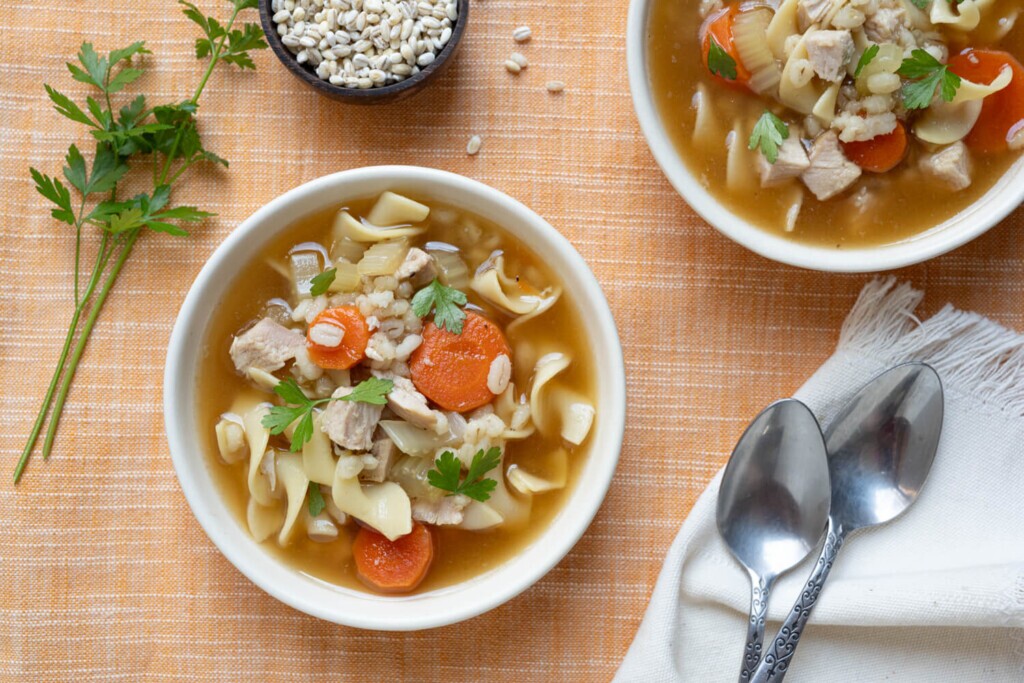 Leftovers Recipe: The image shows two bowls of turkey barley noodle soup made with leftover turkey, fresh carrots, barley, and egg noodles.