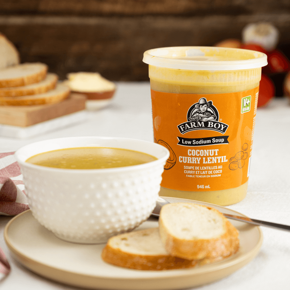 Farm Boy™ Coconut Curry Lentil Soup container and soup in white bowl on white plate with two slices of fresh baguette.