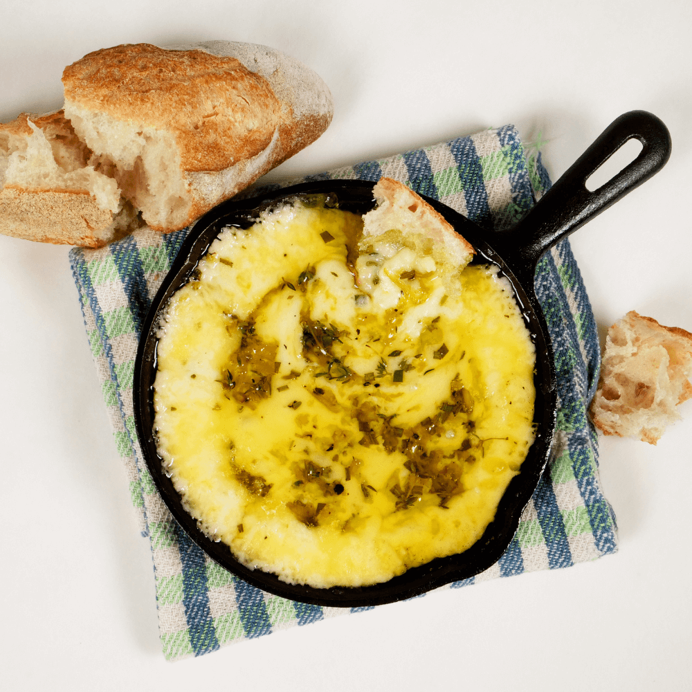 Overhead image of a cast-iron skillet fileld with a gooey baked fontina cheese dip next to some torn crusty baguette.