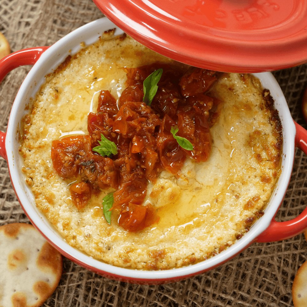 Overhead image of a small red cooking vessel filled with a baked cheese dip.