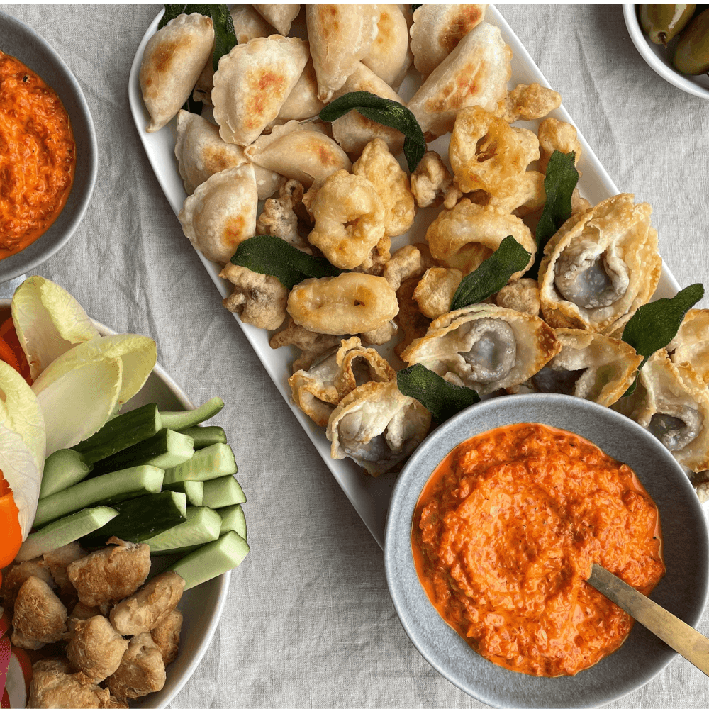 Overhead image of table filled with appetizers like fried wontons and crudites, as well as two bowls of vegan red pepper dip.