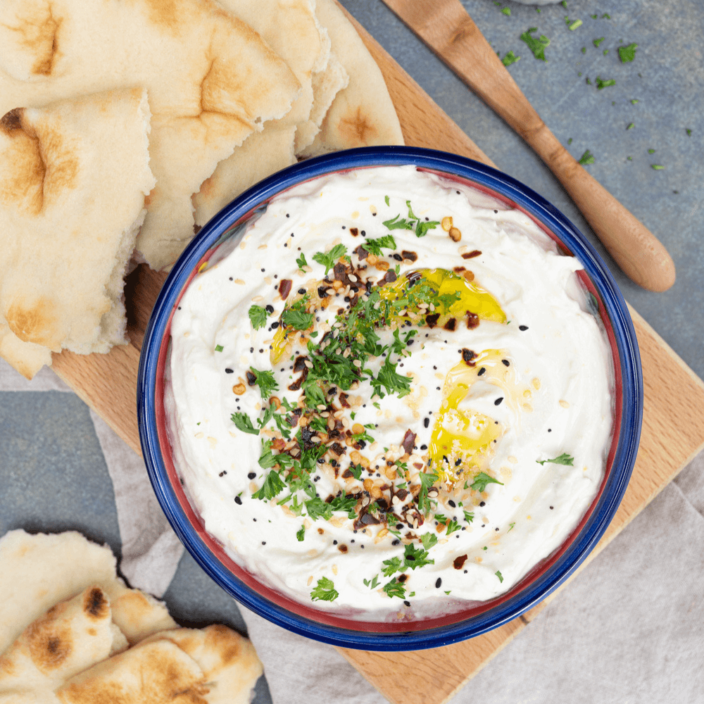 Overhead image of blue-rimmed bowl on a cutting board filled with a whipped feta spread garnished with parsley, olive oil, and spices.