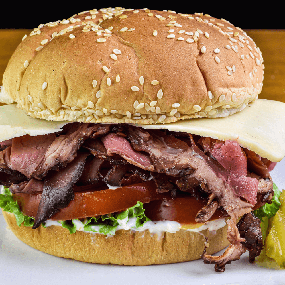 Roast beef sandwich with lettuce, tomato, and cheese on a sesame seed bun.