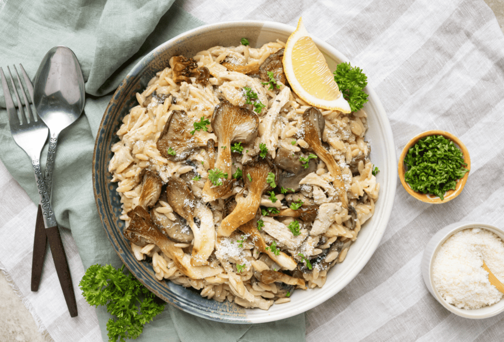 Overhead image of skillet filled with turkey mushroom orzotto made with leftover turkey. Garnished with a lemon wedges and fresh curly parsley.