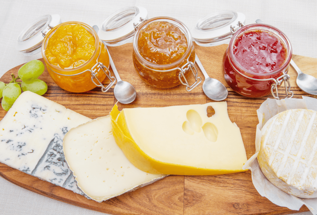 selection of cheeses and jams with grapes on wooden serving board