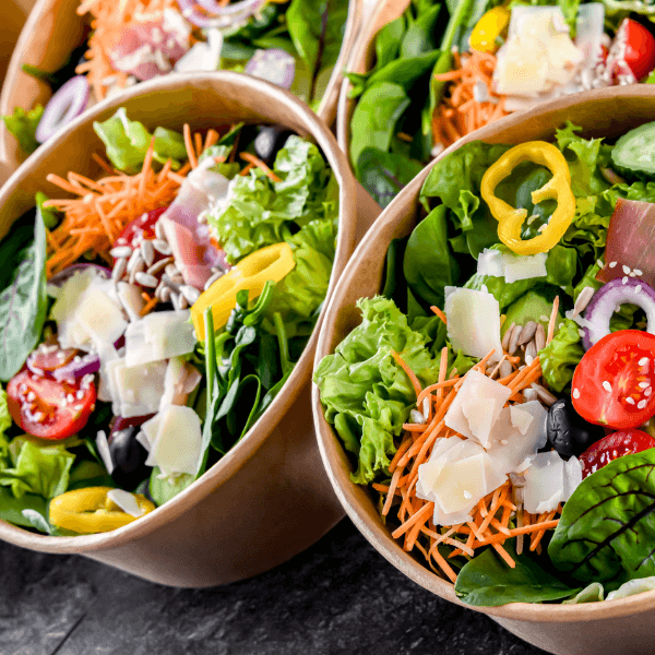 Closeup of multiple cardboard salad bar containers with fresh vegetables.