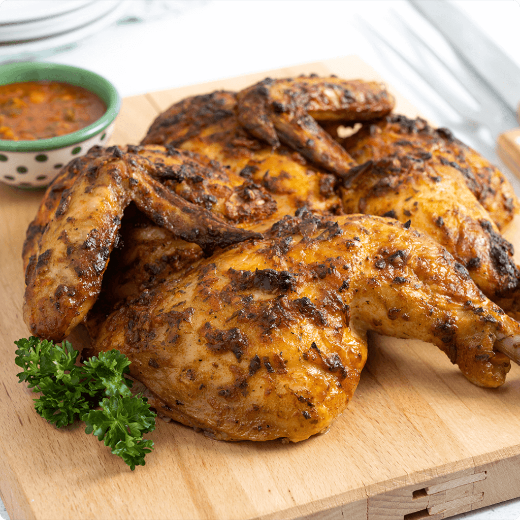 A close-up photo of flattened, marinated piri piri chicken on a cutting board. The chicken is red in color due to the piri piri spices.