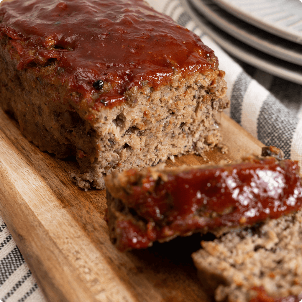 
The image shows a ready-to-cook meatloaf available at Farm Boy. It appears to be a traditional meatloaf topped with a ketchup or barbecue sauce glaze, sliced and ready to serve.