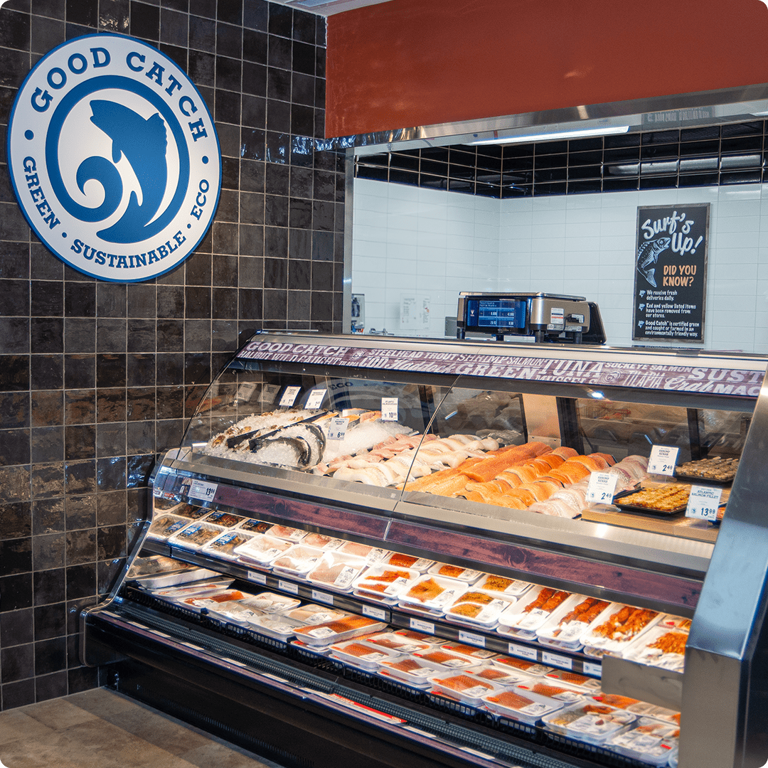 The image shows a seafood display at the Farm Boy Dupont location. The section is branded "Good Catch," emphasizing green, sustainable, and eco-friendly practices. The display case contains a variety of fresh seafood items, including fish fillets, shellfish, and sushi-grade fish. Above the display, a sign highlights information about sustainable fishing practices. The overall presentation is clean and organized, showcasing the freshness and quality of the seafood products available.