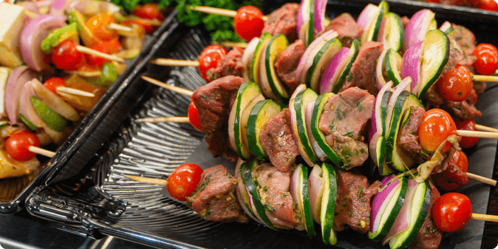 A close-up of a chicken skewer with cubed chicken, vegetables, and bell peppers threaded onto skewers and grilled. The kebab is served on a plate. 