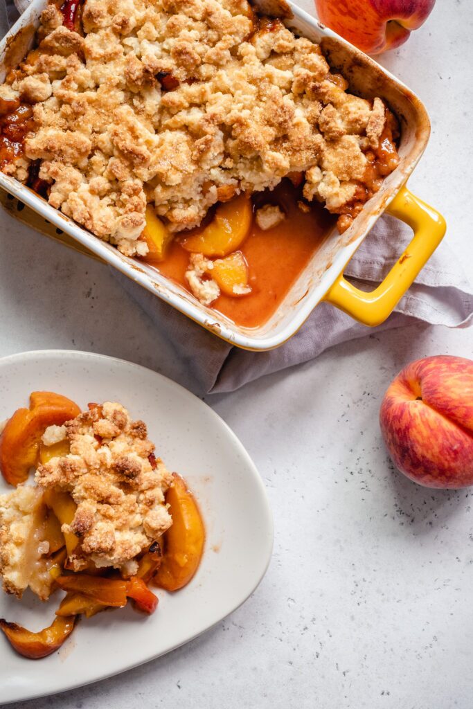 A casserole dish filled with peach cobbler next to a plate of peach cobbler. 