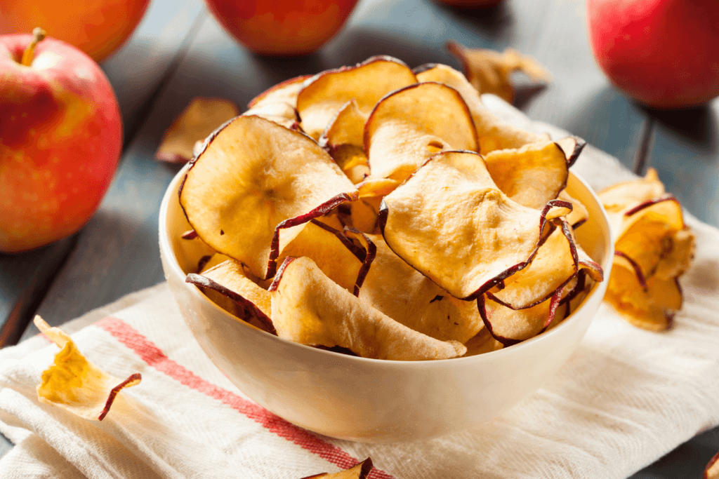 white bowl of apple chips on red and white striped tea towel with whole apples in the background.