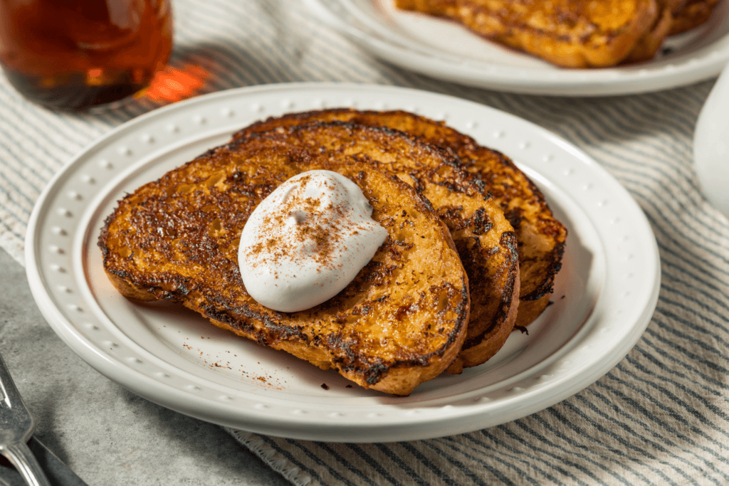 Three slices of eggnog French toast on white plate with decanter of maple syrup in the background.