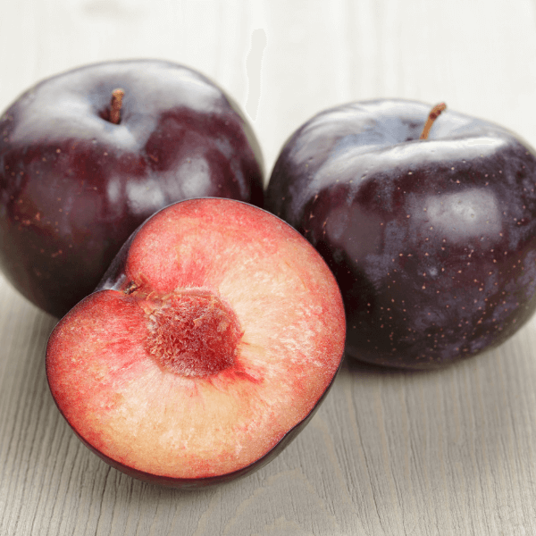 Slice and whole black plums on light wooden table.