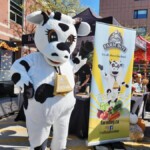 Farm Boy's mascot Lulu standing with a festival banner.