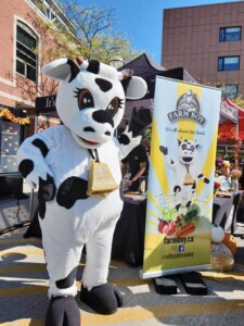 Farm Boy's mascot Lulu standing with a festival banner.