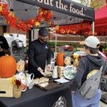 A Farm Boy employee surrounded by fall decor offering a customer a free food sample.