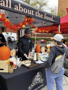 A Farm Boy employee surrounded by fall decor offering a customer a free food sample.