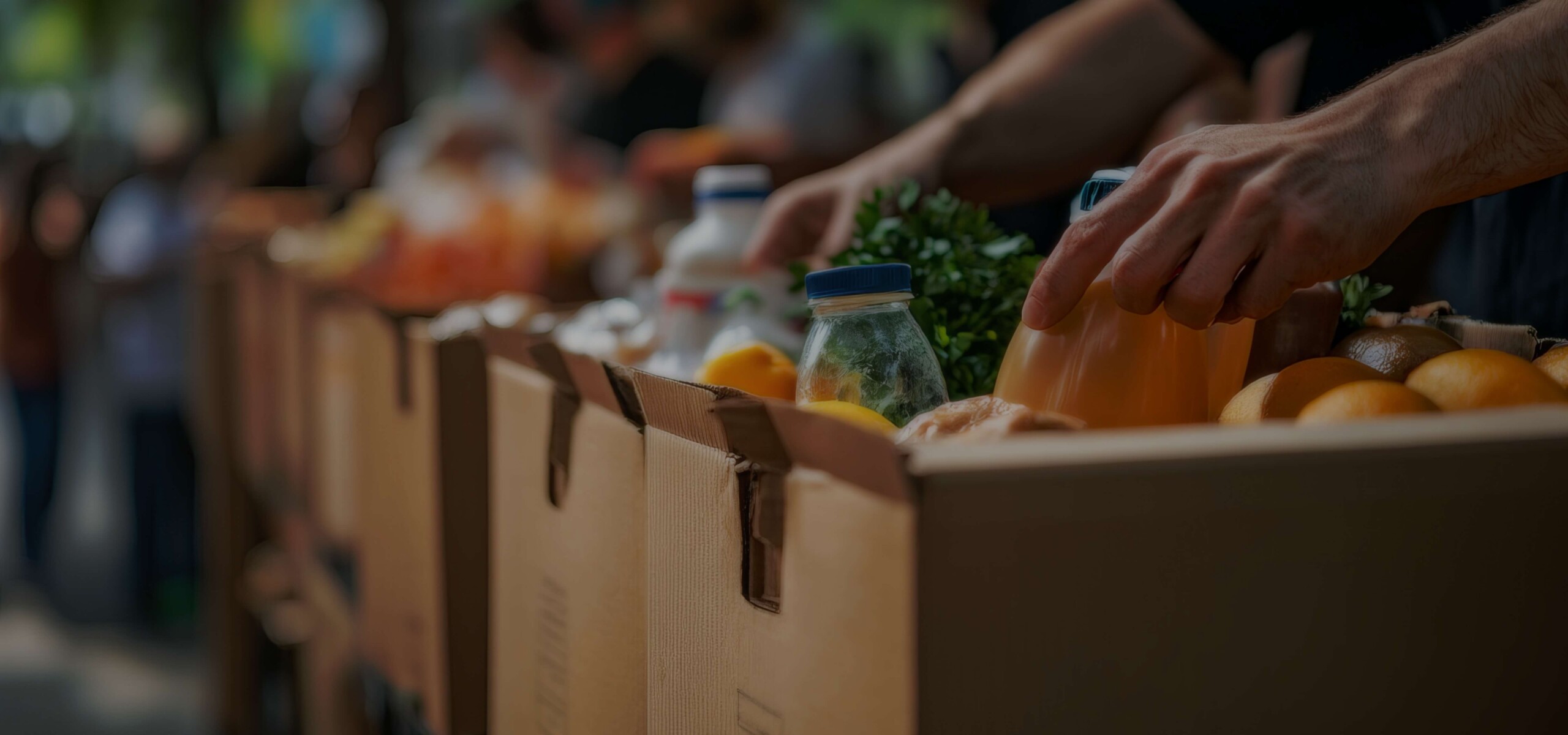 A person placing food into a box along with others in the background.