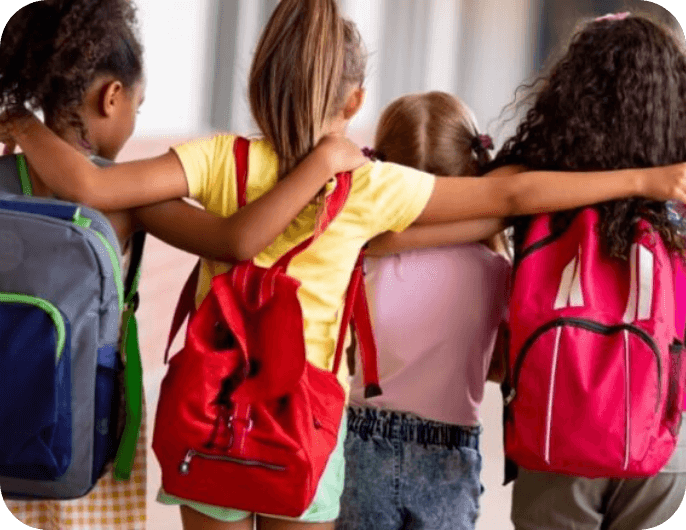 Four girls walking together with their arms around each other, wearing colourful backpacks and walking down a school hallway.