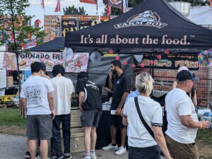 A small crowd of people walk by the event table. A few people stop to sample the free drinks.