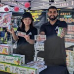 Two Farm Boy employees hold up the Farm Boy drinks while posing for a photo.