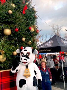 Farm Boy's Lulu the cow and a farm hand standing beside a huge Christmas tree.