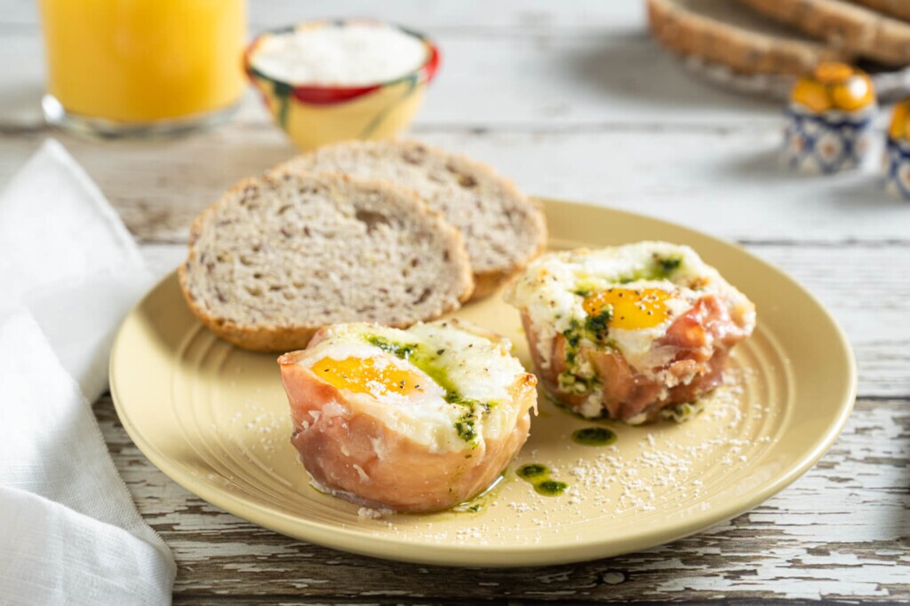 yellow plate with two slices of bread and two cheesy breakfast egg bites with prosciutto and pesto.