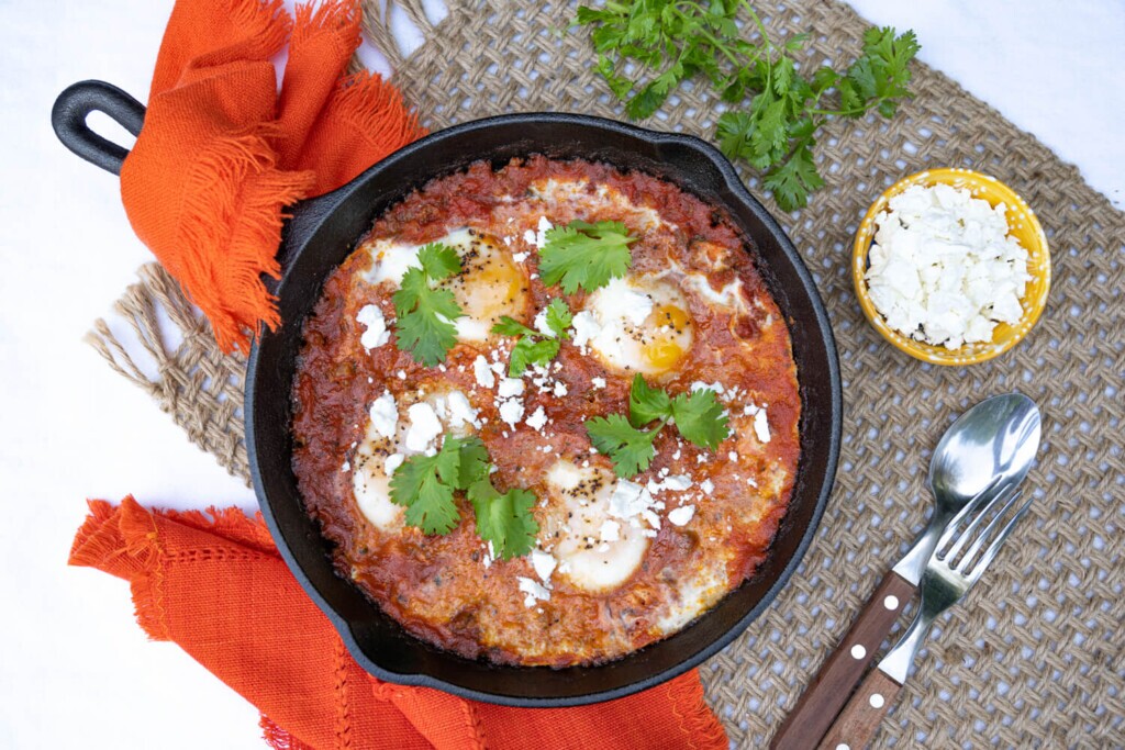 Overhead image of a cast iron pan filled with saucy skillet eggs for brunch or breakfast.