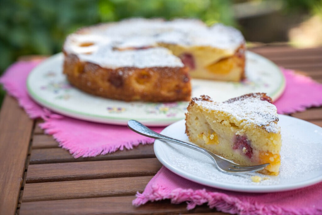 Plate of brunch summer fruit coffee cake with a slice cut out and placed on another smaller plate at the forefront.