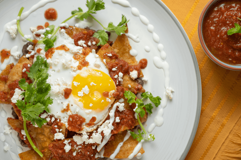 Overhead image of a plate with red breakfast chilaquiles garnished with cheese, salsa, and fresh cilantro.