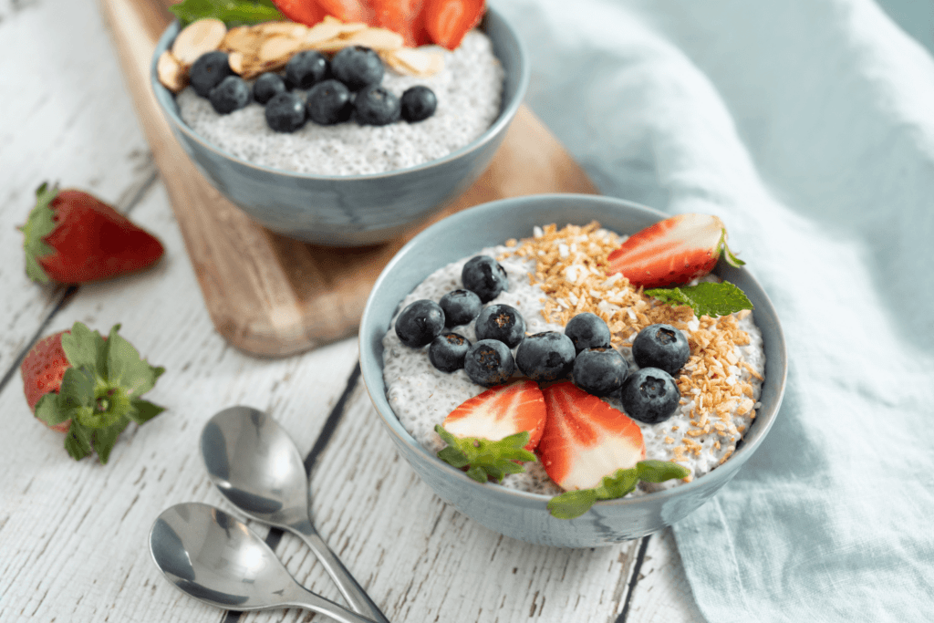 Brunch Recipe: two blue bowls of coconut chia pudding garnished with fresh strawberries, blueberries, and toasted coconut.