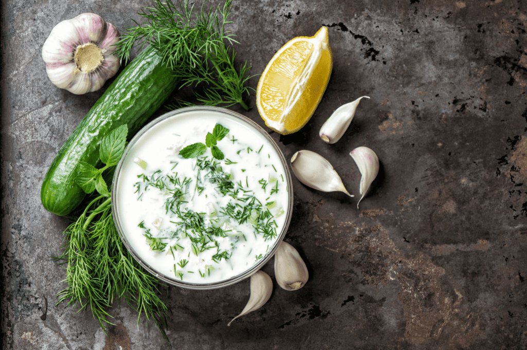 fresh tzatziki on dark background with lemon, garlic, cucumber, and dill